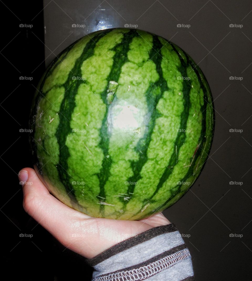 Hand holding a watermelon ona dark room.