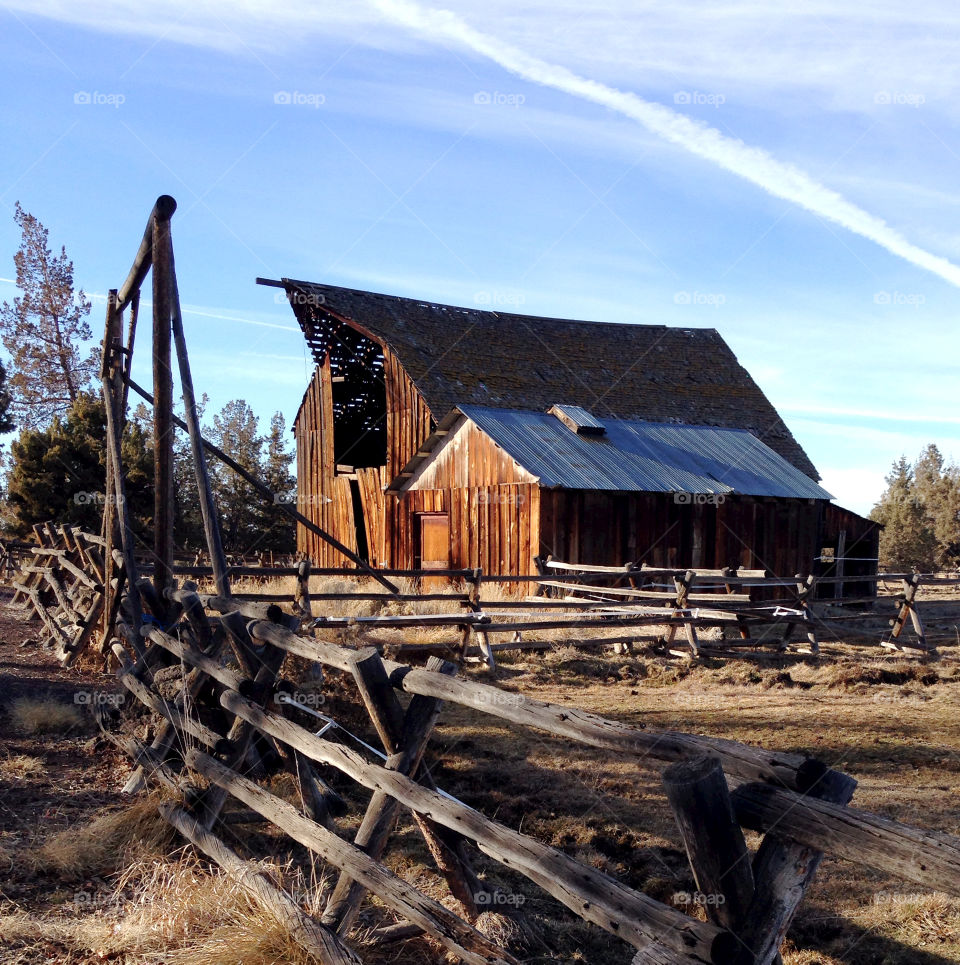 An old wooden barn in a field with a wooden fence surrounding it on a sunny but cold winter morning in rural Central Oregon. 