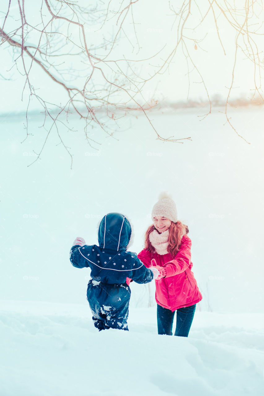 Teenage girl enjoying snow with her little sister. A few years old girl is walking through deep snow while snow falling, enjoying wintertime. Children spending time together. Girls are wearing winter clothes