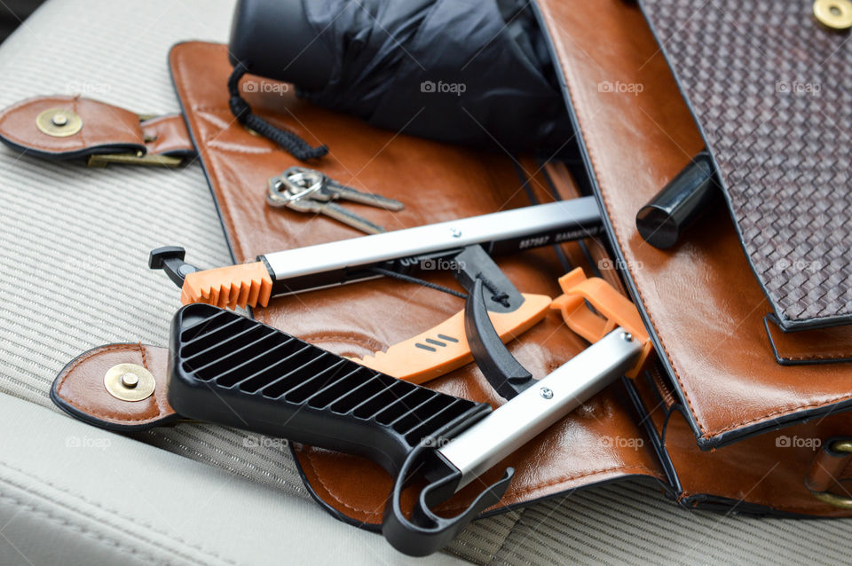 Purse laid out on the seat of a car with a foldable reacher inside