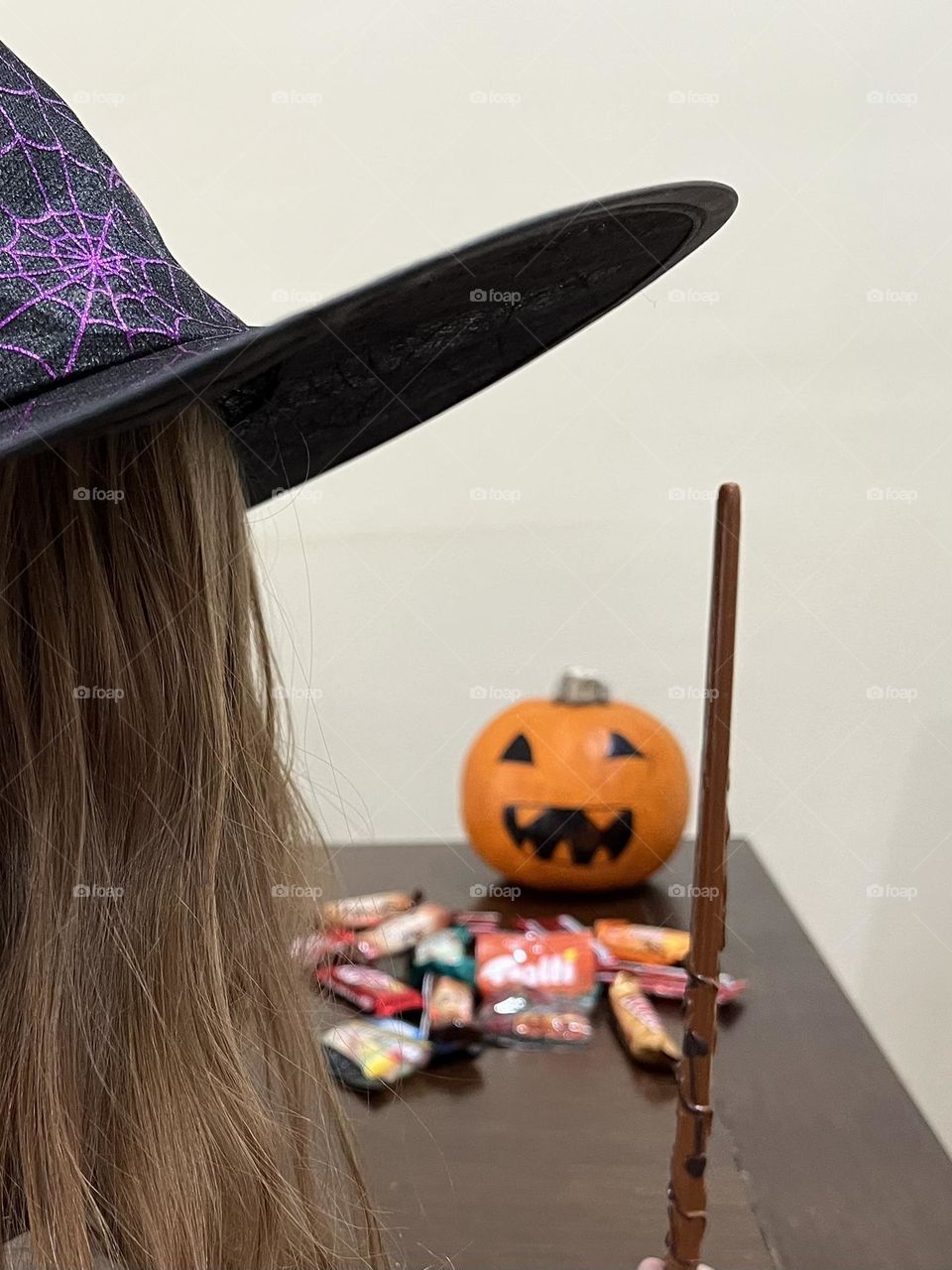 Girl in a witch’s hat and wand anticipating eating candy..