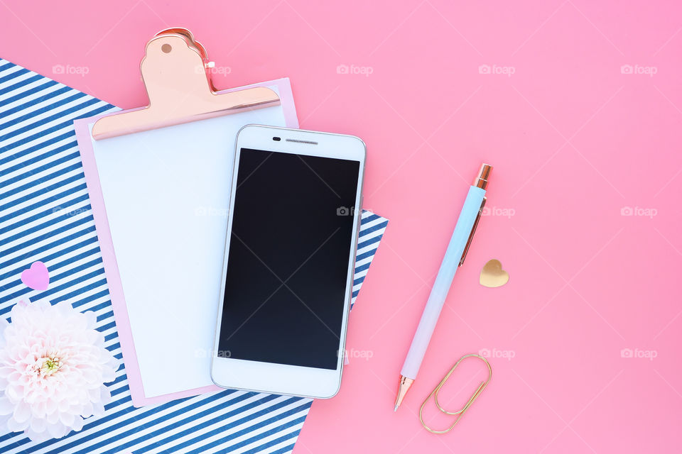 smartphone, blackboard with clip, pen and paper clip on pink background