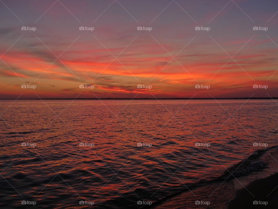 Radiant Sunset over the calm bay. Colorful clouds reflect in the water giving it a reddish purple reflection