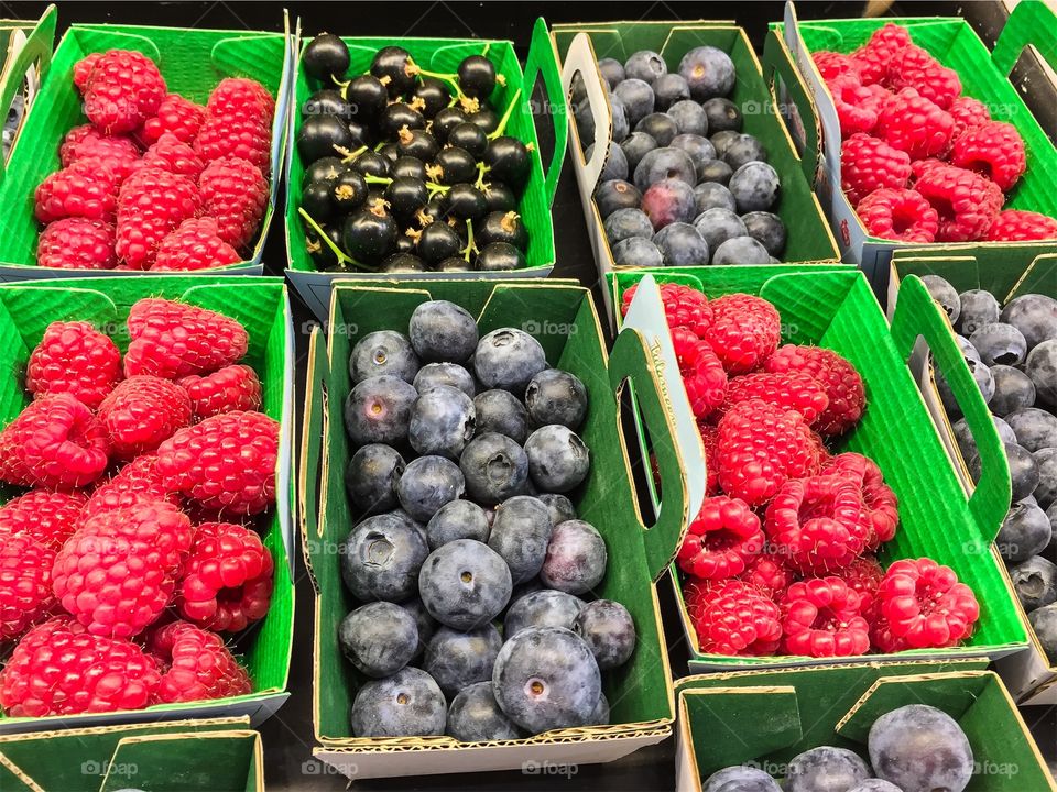 Close up of fresh harvested blueberries and raspberries and black currant in fruit boxes ready for sale at farmers market.