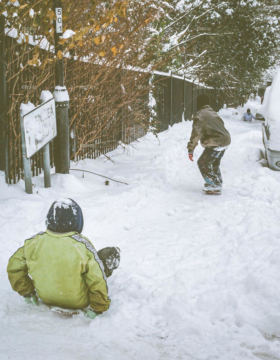Youngsters snowboarding down a hill in a residential area