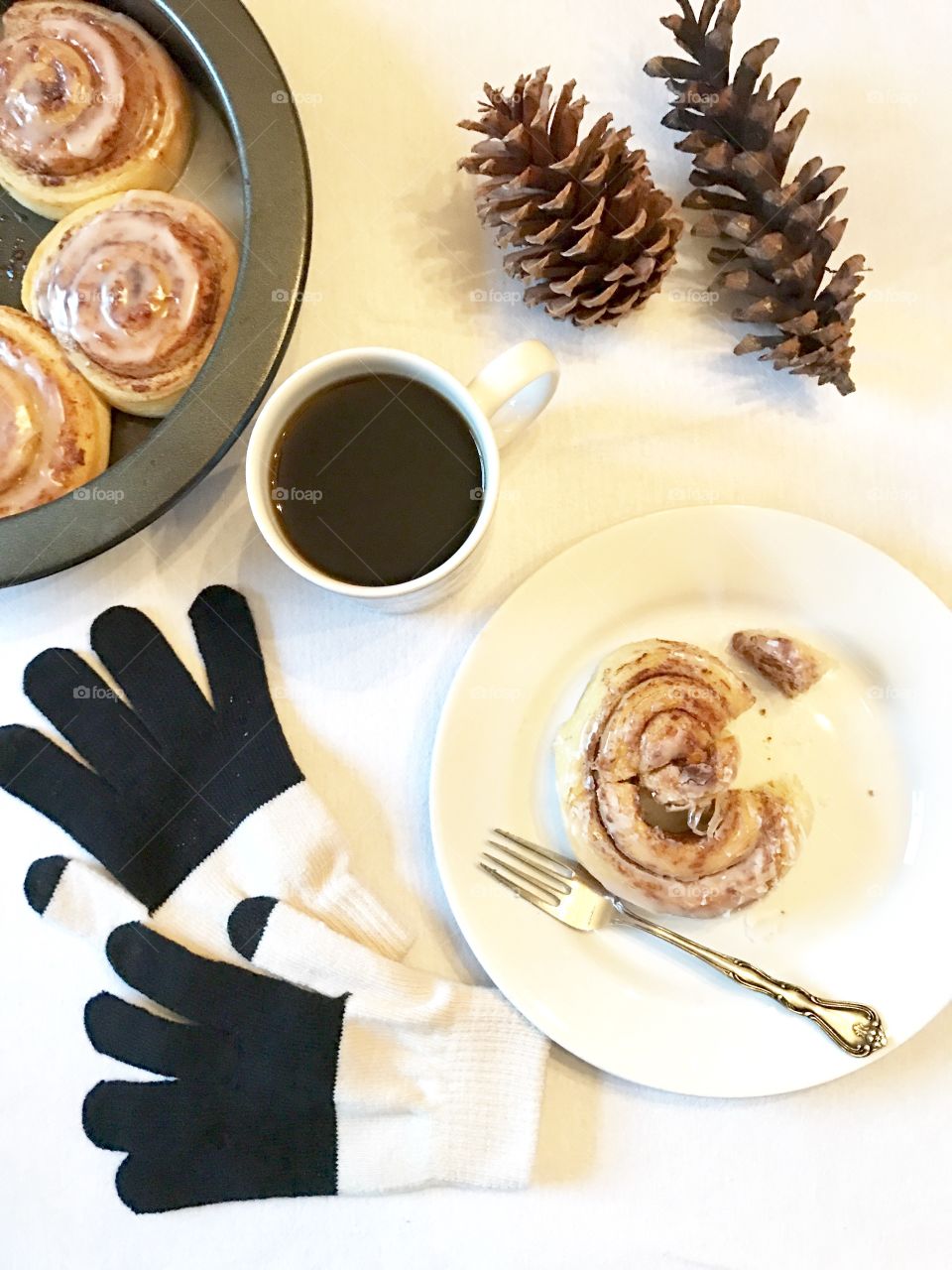 Cinnamon Rolls, coffee, gloves and pine cones on white
