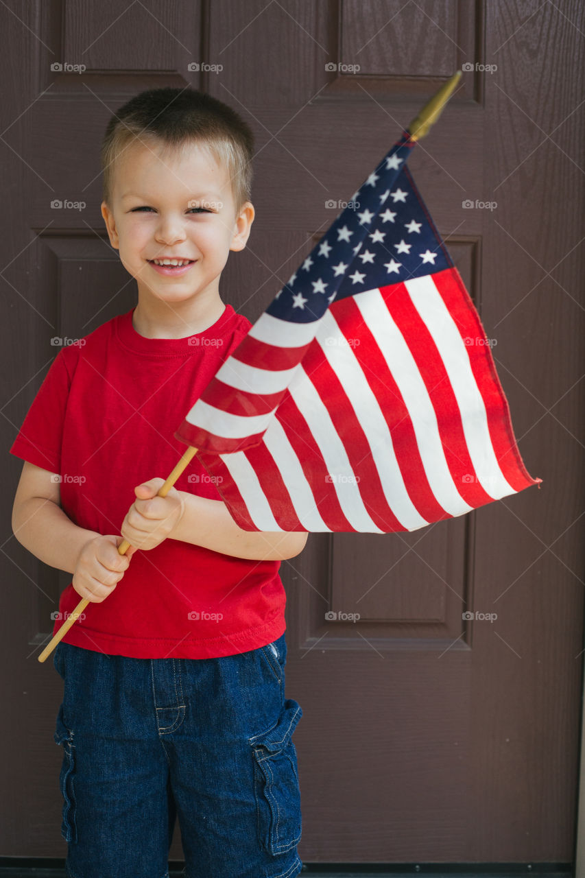 Young boy holding USA flag in front of his door to the house