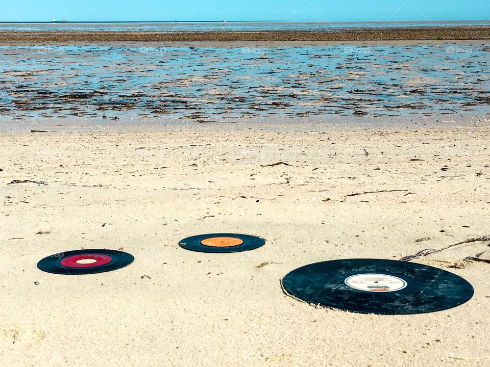BeXh scene vinyl vintage records LPs 45s on sand at beach at ocean waged up on shore
