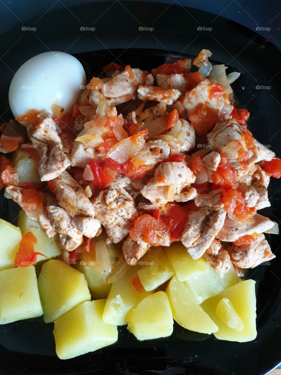 Healthy food. Chicken breasts seasoned with pepper and oregano, with tomatoes and onions, boiled potatoes and a boiled egg on a black glass plate