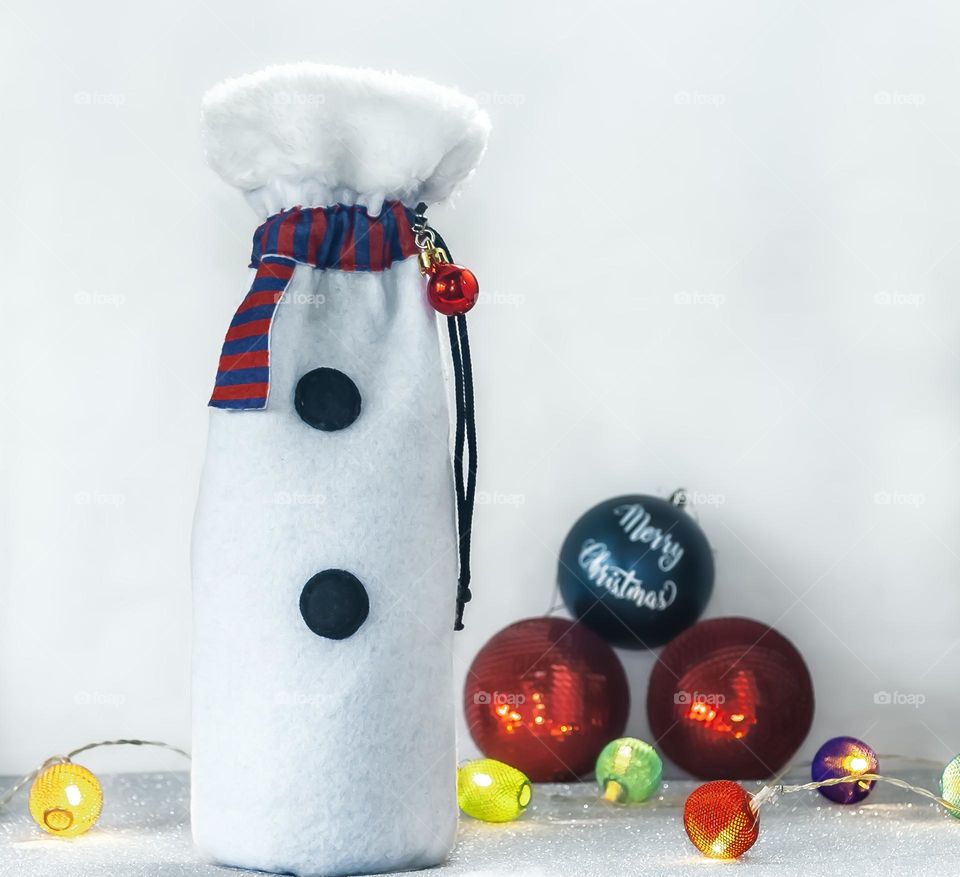 A bottled of wine in a snowman themed gift bag, with lights and baubles