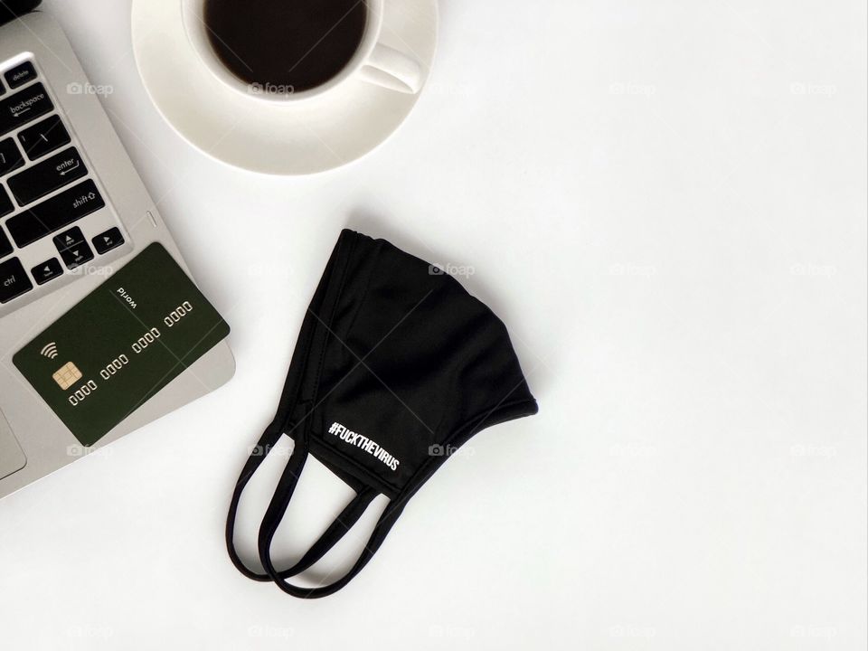 Laptop keyboard, credit card, black face mask with the inscription "fuck the virus", a cup of coffee. Online shopping.
