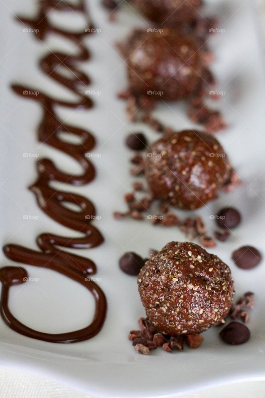 More Chocolate - Nut Butter Cocoa Bites on rectangular white dish with scattered cacao nibs and chocolate chips, and the word "Chocolate" written in chocolate drizzle