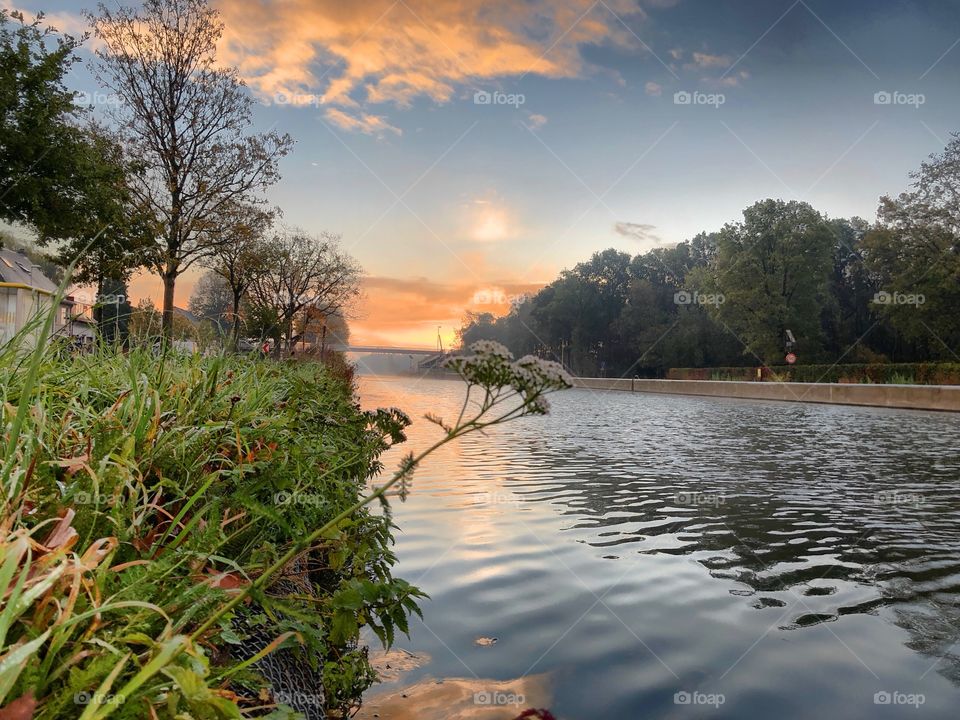 Soft sunrise over a Countryside landscape reflected in the water of the river as seen from the Grassy riverside.