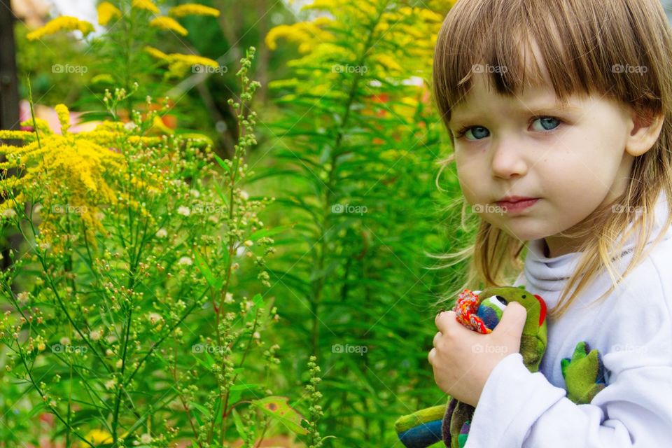 Little girl with toy frog on a background of autumn flowers