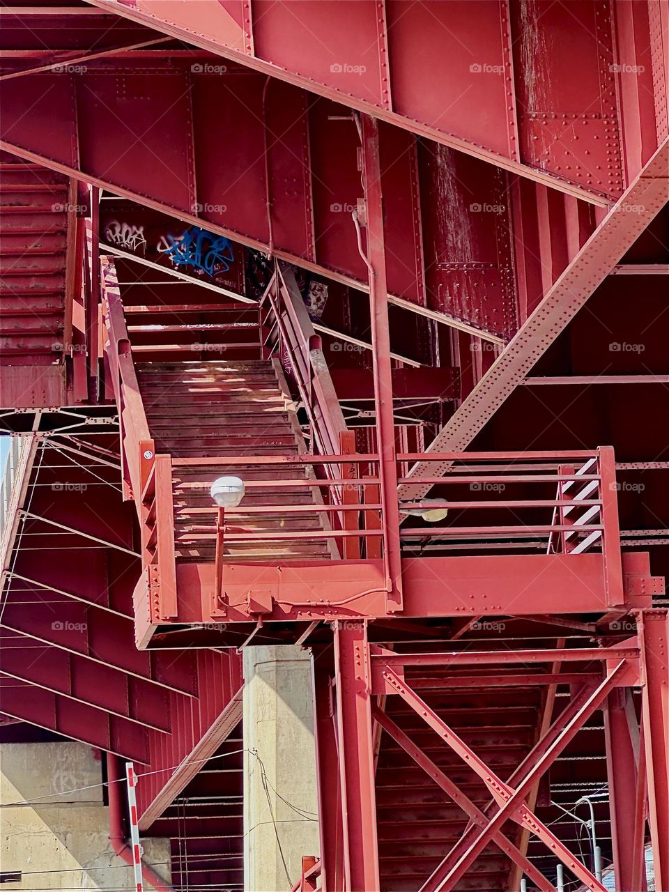 This is a closeup of the red metal staircase of the “Pulaski Bridge” at “Newtown Creek” in LIC, Queens with its “Bauhaus” inspired industrial minimalist aesthetic, functional design, use of simple geometry and prime color. 2024. Hypnotic Productions