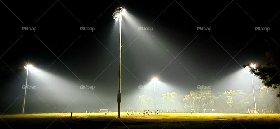 Stadium light towers reflectors against black background. Flood lighting for stadiums surround the circular turf ground. To provide proper illumination, high power high mast.