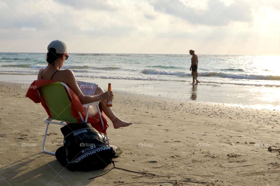 Woman sit on a chair at the beach drinking beer and read magazine 