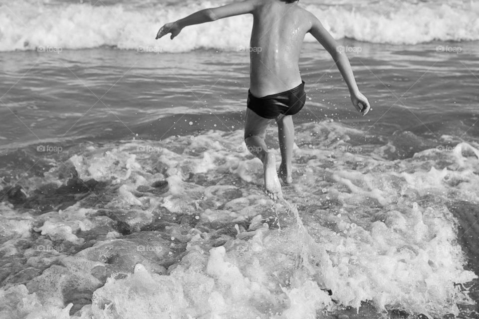 Black and white photo of a kid jumping waves in a beach