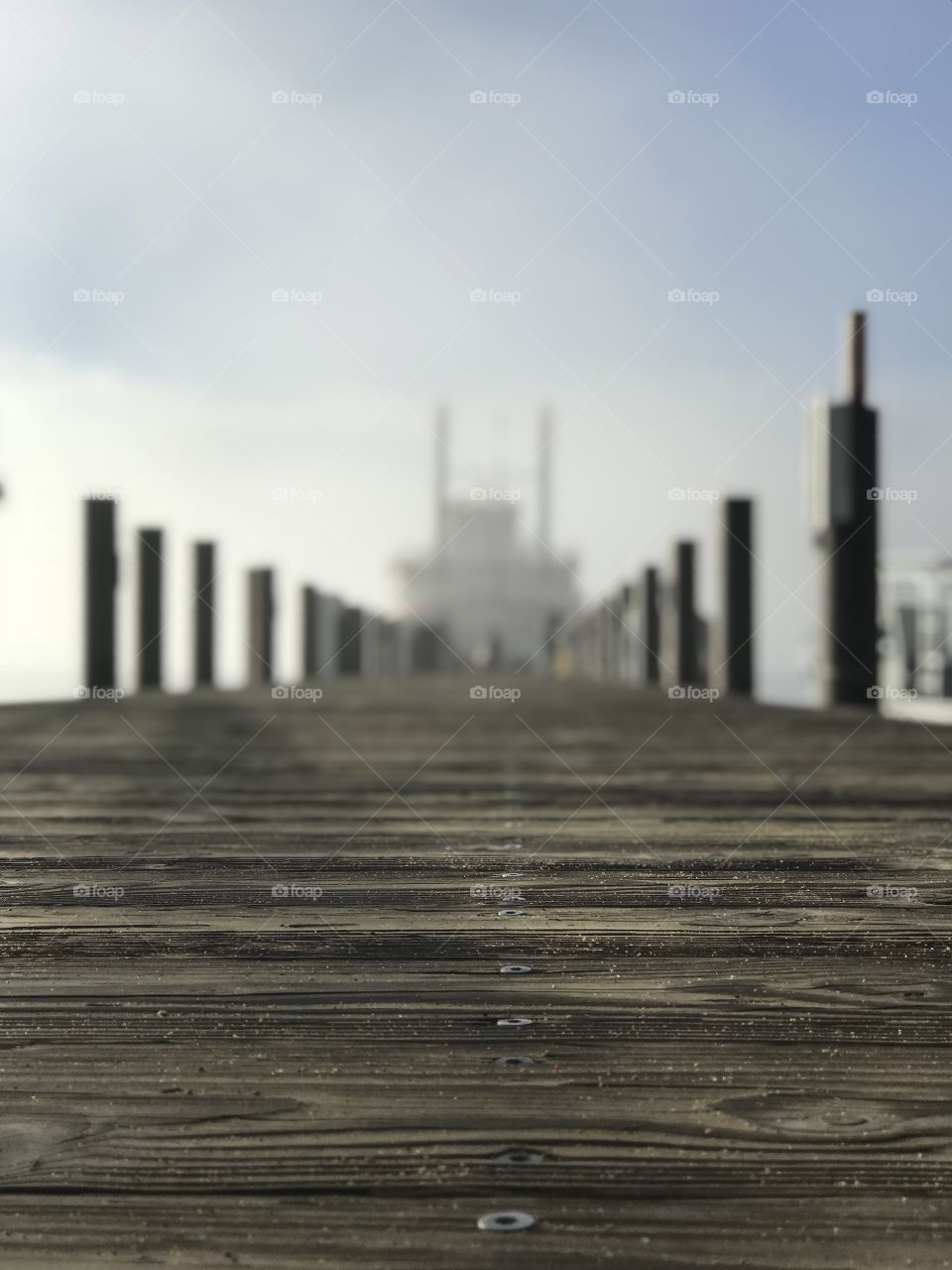 A closeup of the dark wood of a dock that leads to a cruise ship in the distance on a fog covered day. 