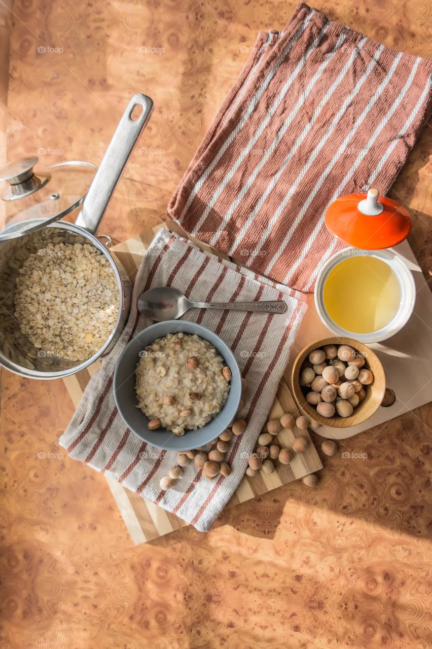 Cooked oatmeal in a deep gray plate with hazelnuts and honey.