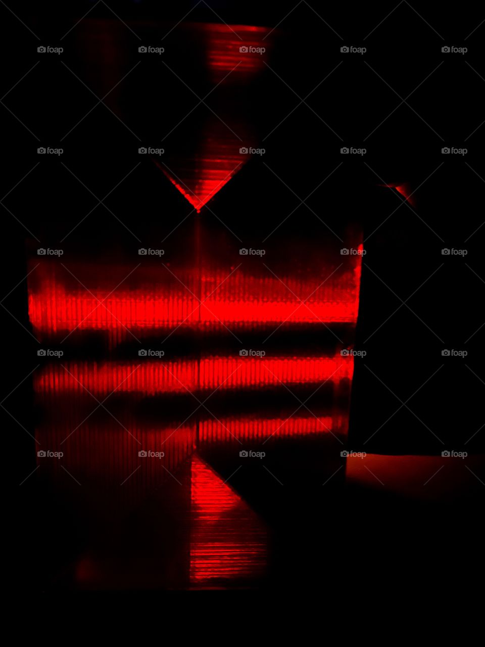 A creepy, vibrant, red picture. A candle burns between a translucent red pane. A hand reaches behind the pane. 