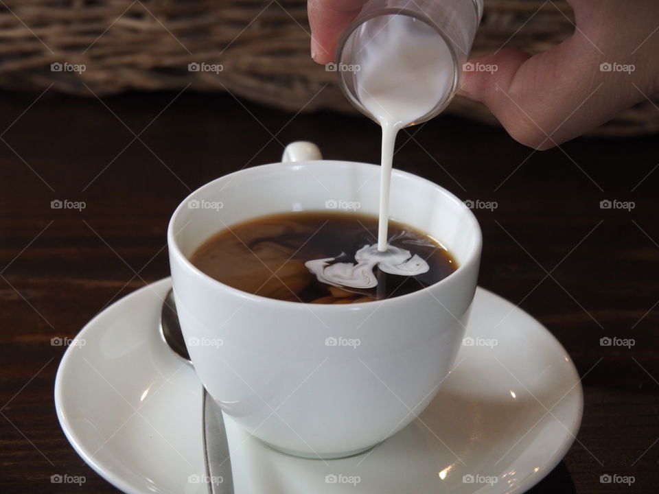 Pouring fresh milk in coffee. The moment of pouring milk in a cup of coffee. It's like freezing time to see how it looks like on the surface of the coffee when we pour the milk in.