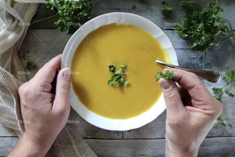 Man sprinkles fresh parsley in Butternut soup