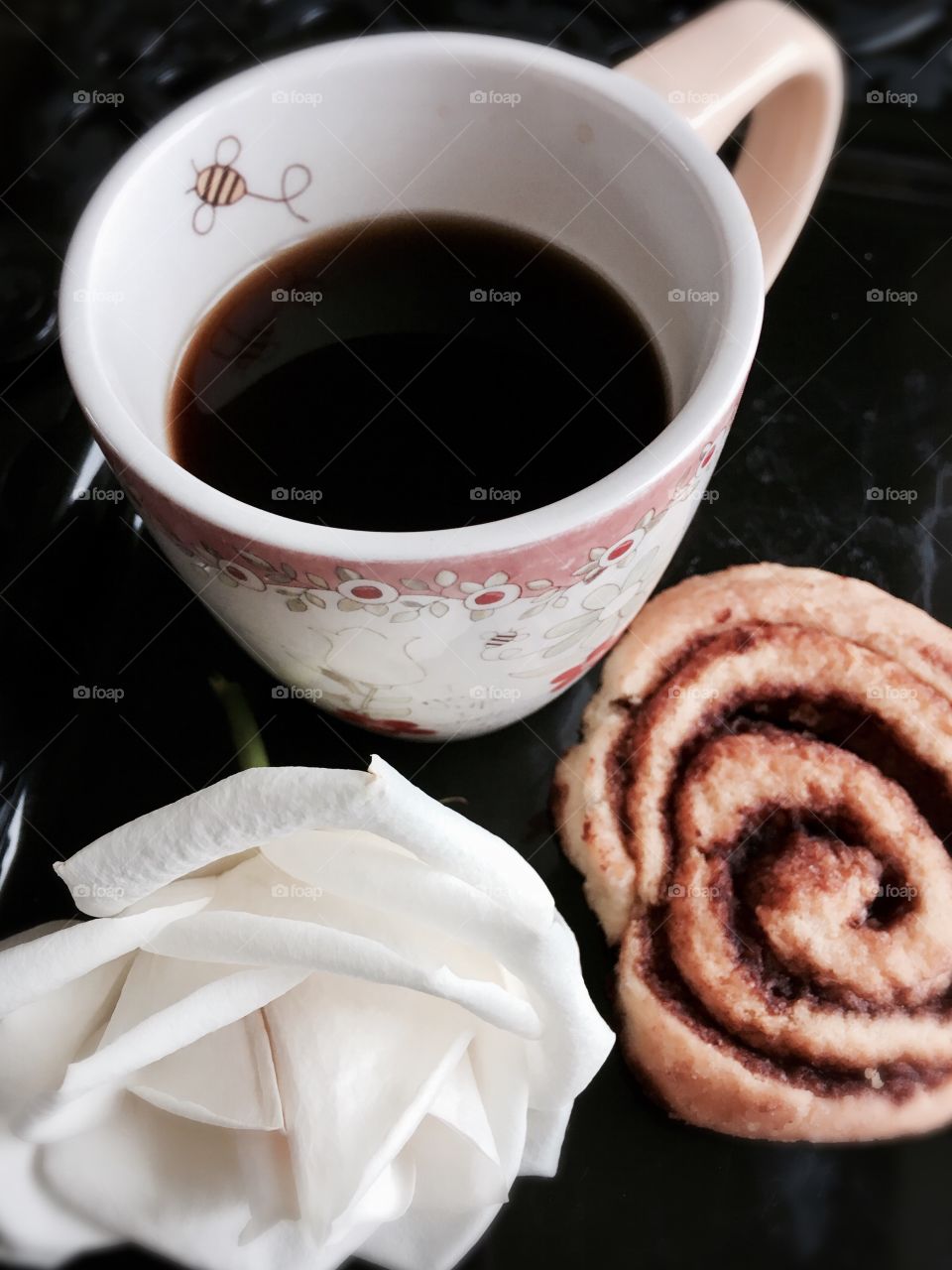 Black coffee, white rose, cinnamon roll. On black tray for breakfast in bed. 