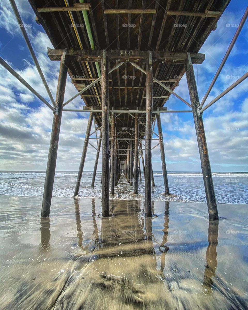 Standing under the pier and the glassy water smooths over the sand 