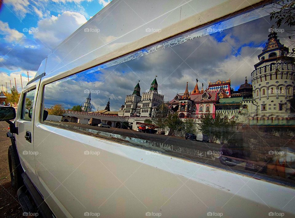 Cars.  The long window of a white limousine, which reflects: the domes of the towers, the blue sky with white clouds