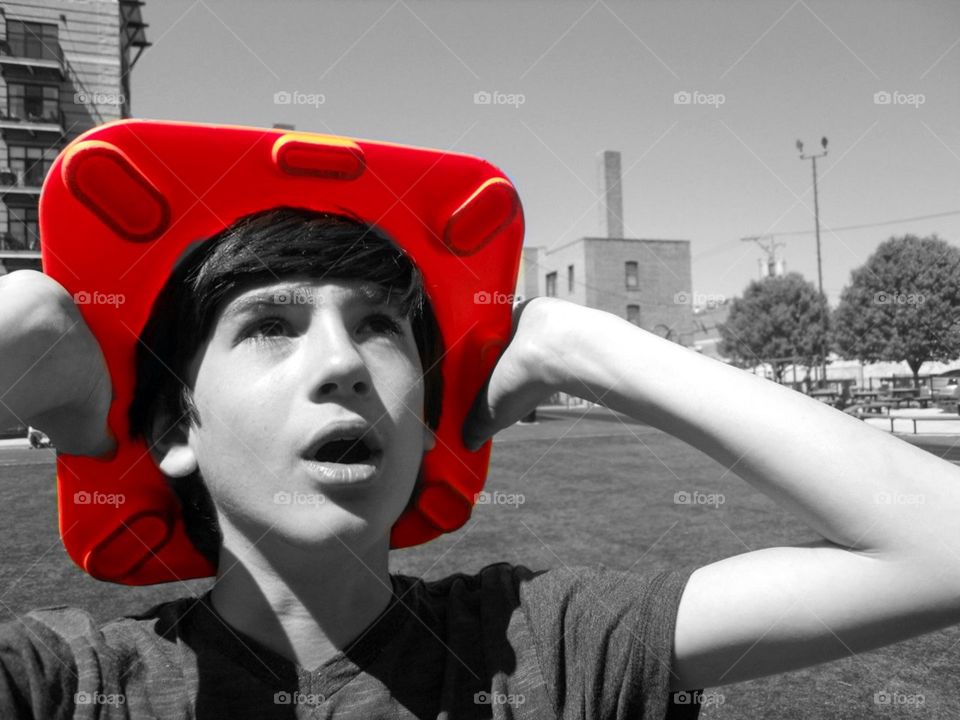 Semi black and white photo of boy with colored orange cone on head looking into the sky 