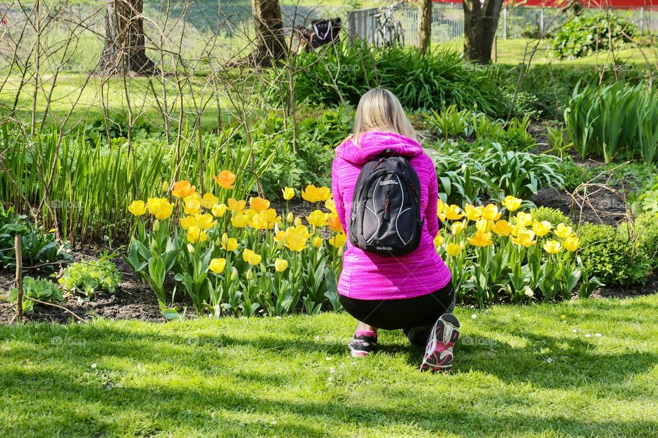 Young blonde girl takes pictures of beautiful yellow tulips in the Park