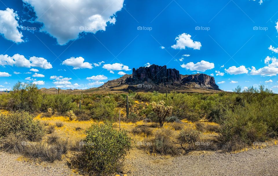 This is a slightly panoramic photo shot near the base of the Superstition Mountains on a rare and glorious cloudy day. There is shadowing from the clouds on the mountain range and shows the desert of Arizona.