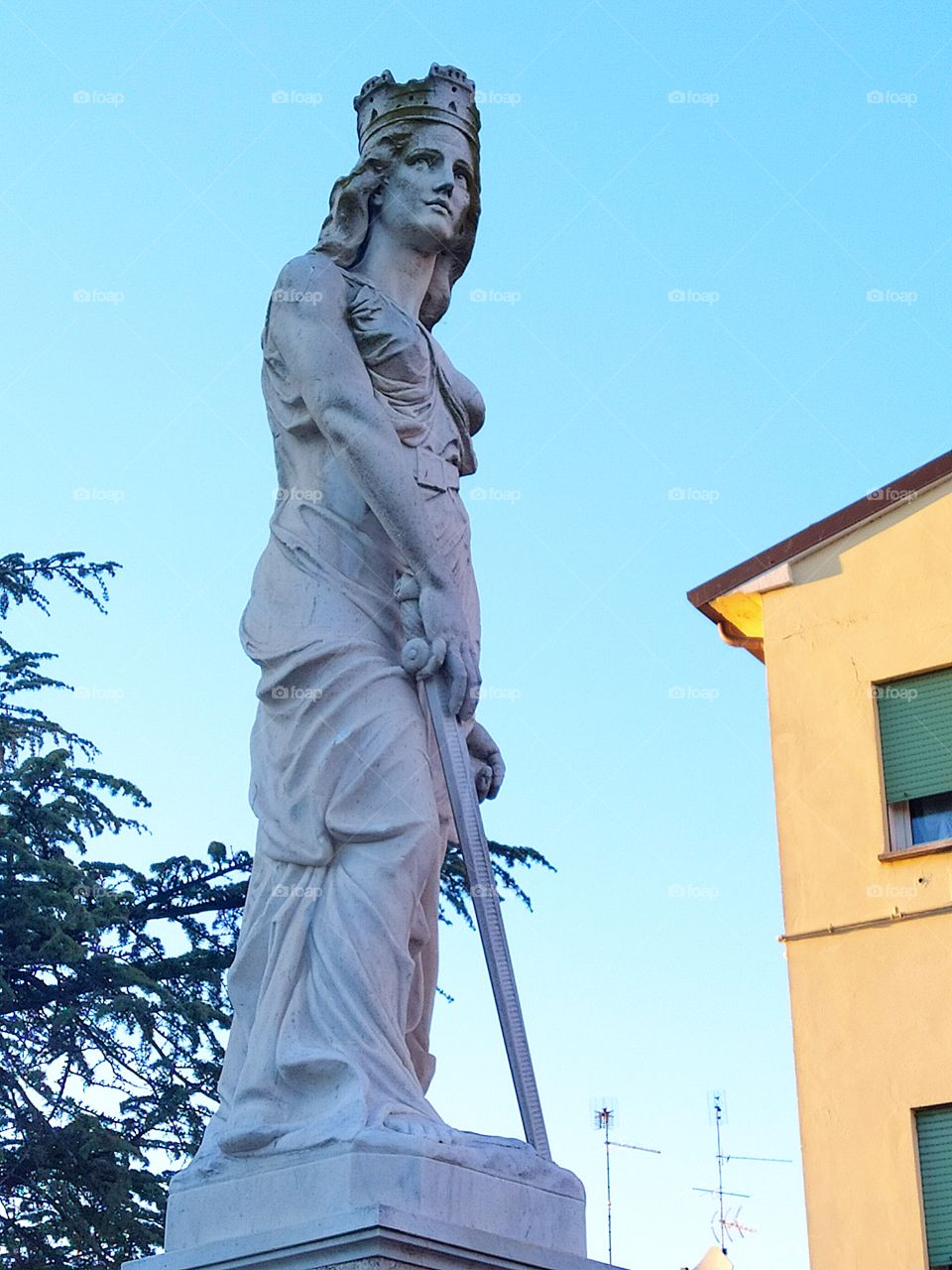 Gray statue of a woman with a sword next to a yellow wall at home. Italy. Veneto region