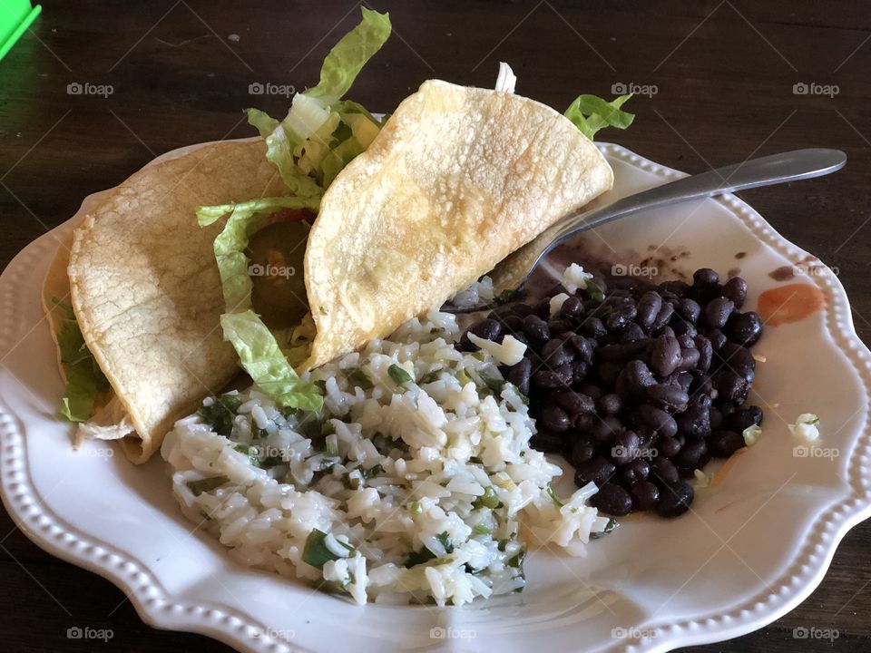 Cilantro lime rice, black beans and chicken and lettuce filled corn tortillas on a scalloped white ceramic plate
