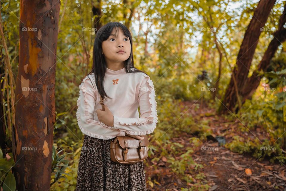 Wandering and admiring the beauty of fall season, environmental portrait of a young little girl in the woods.