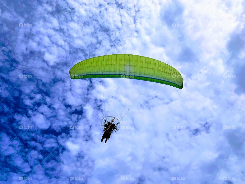 green paraglider flying in the clouds