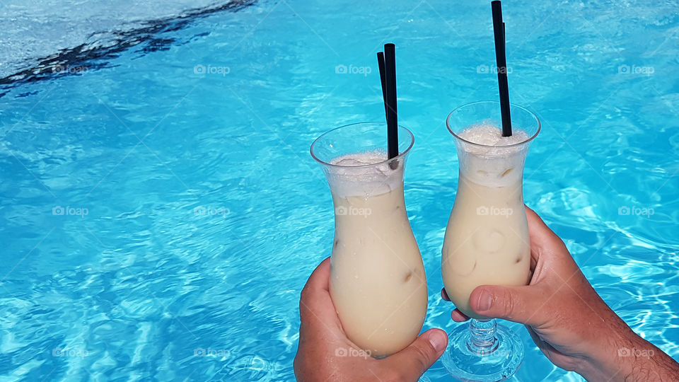 Holding  pina colada drinks in the pool 
