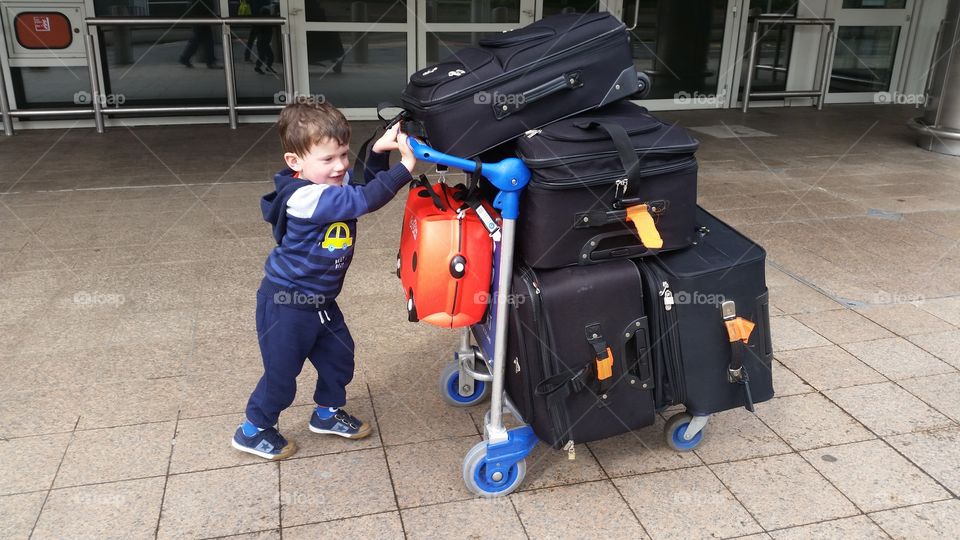 Young boy pushing a big pile of suitcases at the airport.
