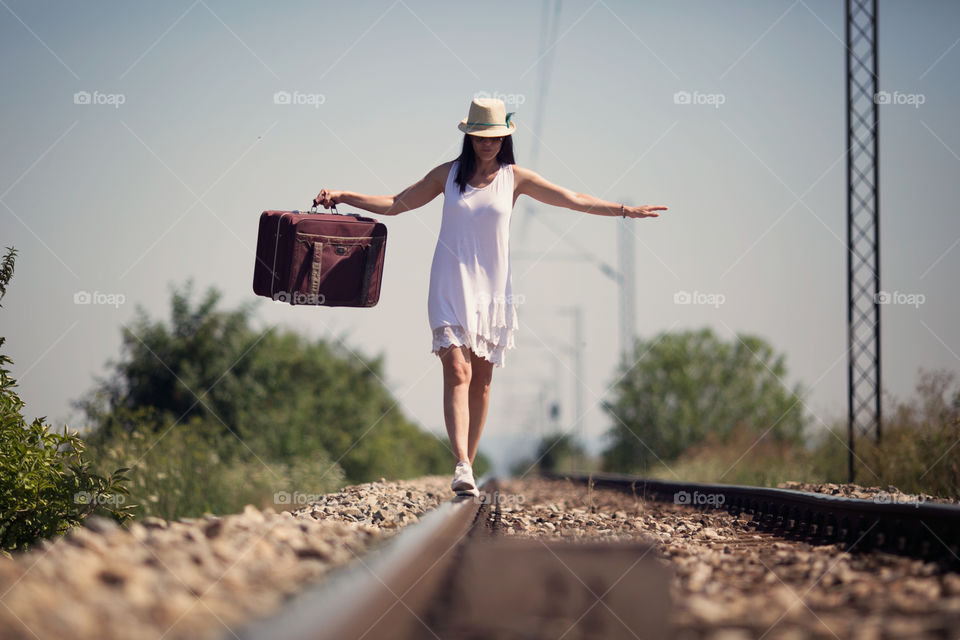Woman balancing on railroad track with holding suitcase