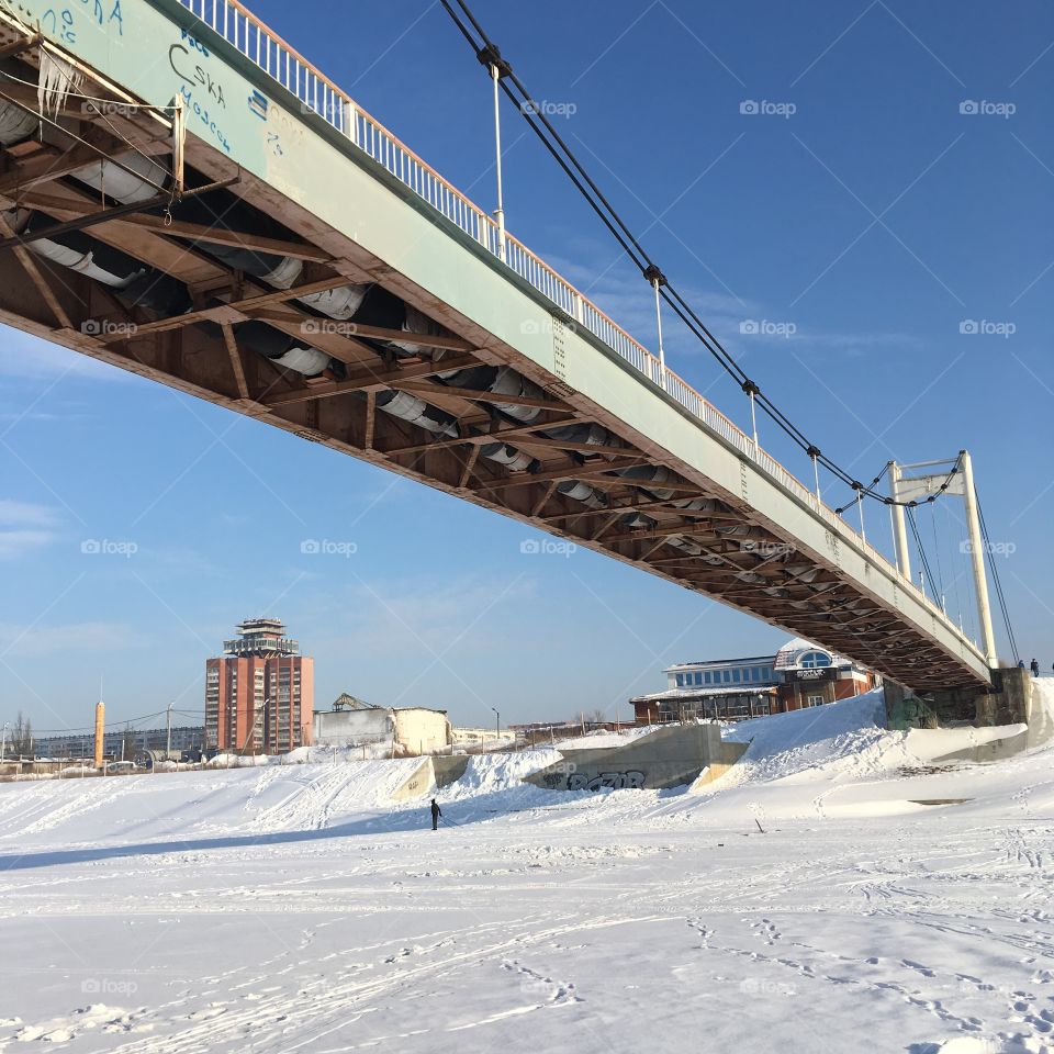 background view from below on an old pedestrian cable-stayed bridge in the city of yoshkar-ol in Mari El, from the ice of a winter river covered with snow