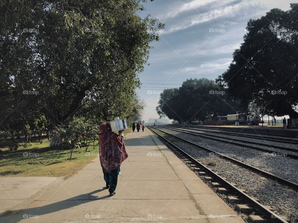 A villager taking cooking pot on her shoulder through railway station platform