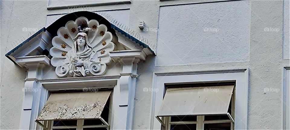 This old fashioned vignette above the entrance to a building in the inner city of “Munich”, capitol of “Bavaria” gives testimony to the beauty and great variety of the architecture here. 2024. Hypnotic Productions