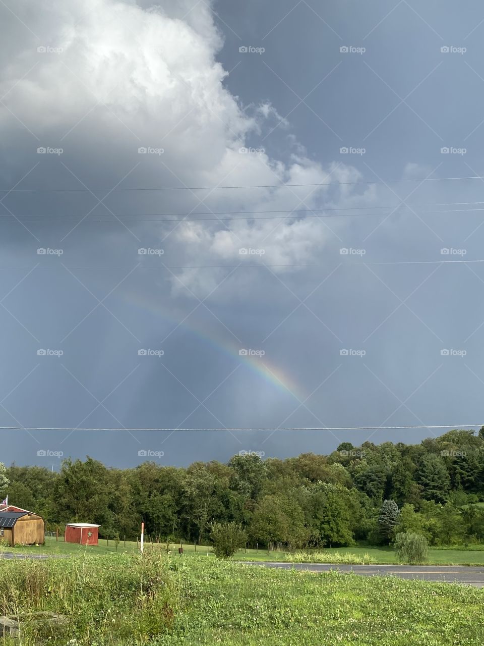 Beautiful dark blue sky with white puffy clouds and rainbow above a green field