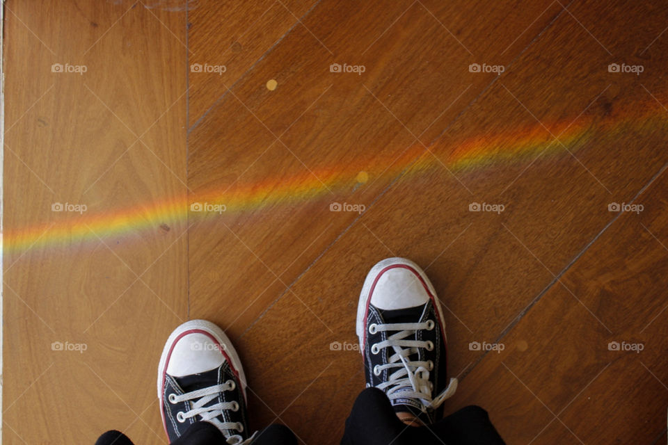 a pair of beautiful sneakers next to a colorful beautiful rainbow projected on a wood floor