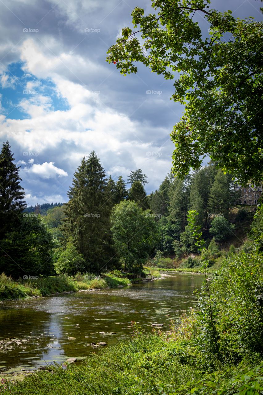 A landscape photo of the semois river in the belgium ardennes. the river is in a forest and surrounded by hills.