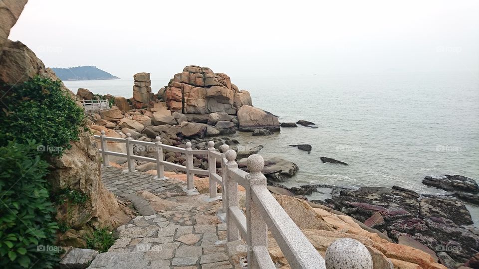 I took this photo during my holiday on 22 of May at around 6:40pm.  A rocky pathway with concrete fence, left above is the huge rocky mountain. right down below is the rocky seashore. this is part of the park located at RUA DE HAC SA LONG CHOW KOK,  Coloane Macau. this park is one among the tourist attraction in Macau