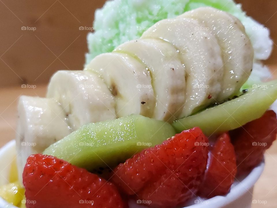 Close up of kiwi shaved ice with fruit.  Sliced strawberries, kiwi, and bananas drizzled with green kiwi syrup.