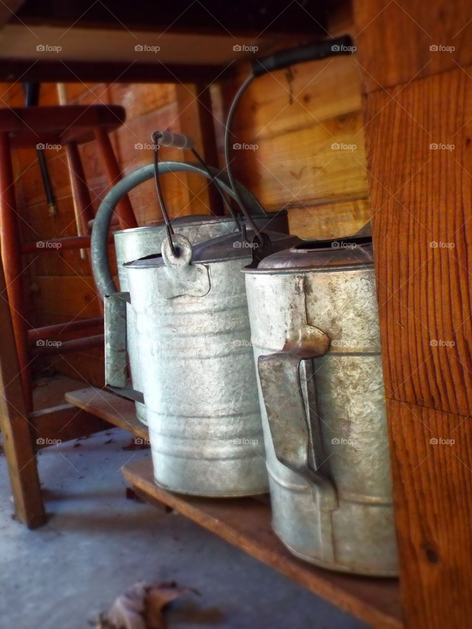 Closeup of vintage rusty galvanized metal watering cans on shelf under potting bench

