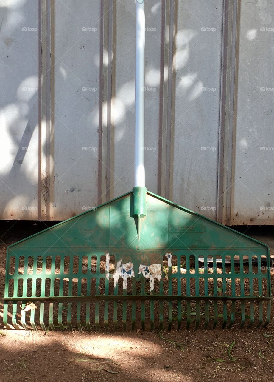 Garden rake leaning up against metal shed; symmetrical vertical lines on both rake, handle, shed 